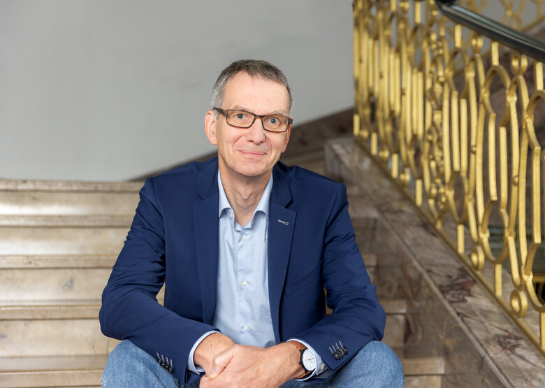 Das Foto zeigt einen Mann auf einer Treppenstufe in einem Treppenhaus sitzend.